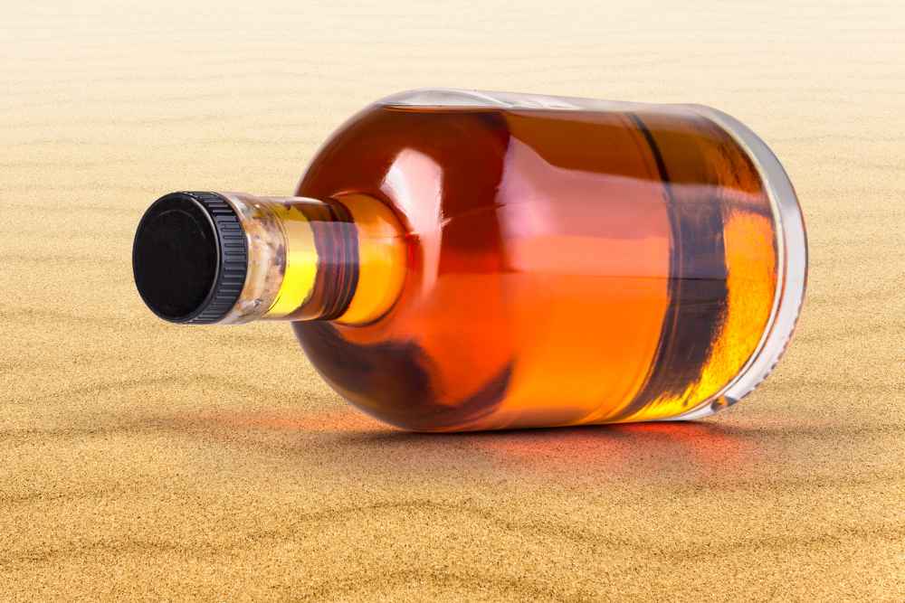 Bottle of Rum on Sand in Sunlight
