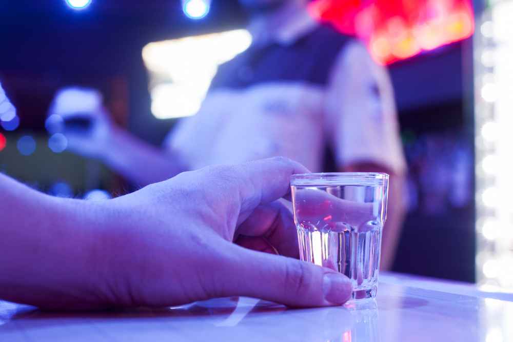 Hand Holding Shot of Vodka on Bar